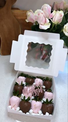 a white box filled with chocolate covered strawberries and marshmallows next to pink roses