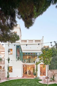 a white house with green balconies and an orange tree in the front yard