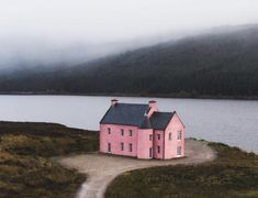 a pink house sitting on top of a lush green field next to a body of water