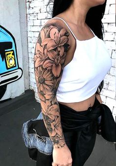 a woman with a flower tattoo on her arm is walking down the street in front of a brick wall