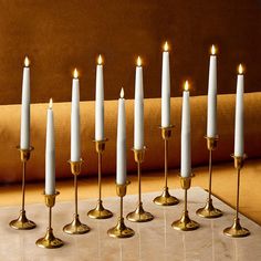 seven white candles are lined up in a row on a marble table with gold accents