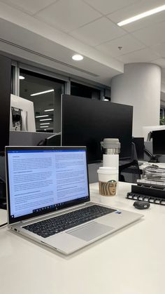 an open laptop computer sitting on top of a white desk next to a cup of coffee