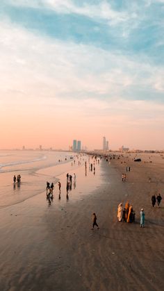 many people are walking on the beach at sunset