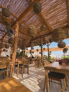 an outdoor dining area with tables and chairs under a straw roof covered in hanging lanterns