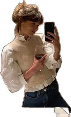 a woman holding a wine glass and looking at her cell phone while wearing a sweater