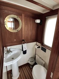 a small bathroom with wood paneling and white fixtures, including a round mirror above the sink