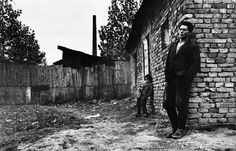 an old black and white photo of a man leaning against a brick wall with his dog