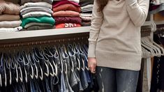 a woman is talking on her cell phone in front of a rack of shirts and sweaters