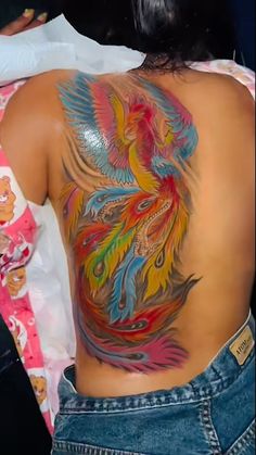 the back of a woman's body with colorful tattoos on her upper and lower back