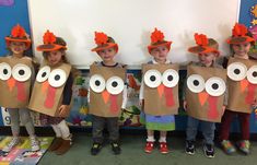 five children wearing turkey paper bags with their faces painted on them and holding up thanksgiving hats