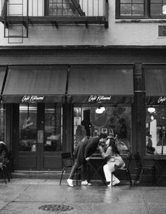 black and white photograph of people sitting at tables in front of a cafe