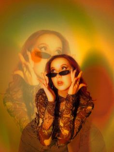 a woman with sunglasses on her face posing in front of a rainbow colored background and holding her hands up to the side