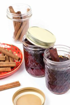 cinnamon sticks and spices sit in glass jars on a white surface next to a red plate