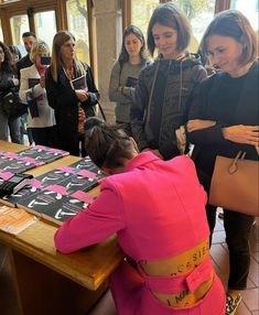 a group of people standing around a table with shirts on it and one woman in pink