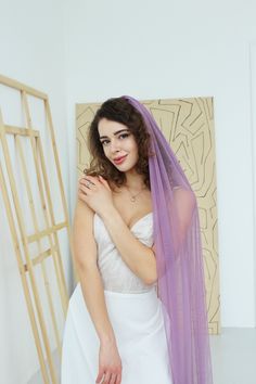 a woman in a white dress is wearing a purple veil and posing for the camera