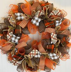 a wreath with orange and brown bows hanging on the front door for halloween decorating