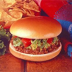 a hamburger with lettuce and tomatoes on it next to some tortilla chips