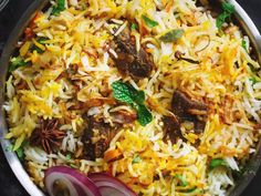 a pan filled with rice and meat next to sliced onions, carrots and cilantro