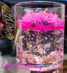 a pink candle in a clear glass with a butterfly sitting on it's side