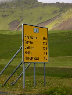 a yellow road sign sitting on the side of a lush green hillside