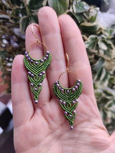 a hand holding a pair of green beaded earrings