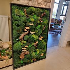 a green moss wall with mushrooms and broccoli in the center is displayed on a white tile floor