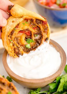 a hand holding a tortilla over a bowl of sour cream and cilantro