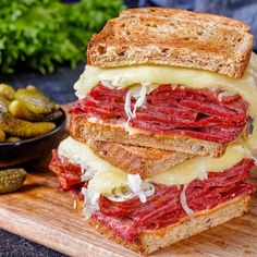 a sandwich with meat, cheese and pickles on a cutting board next to it