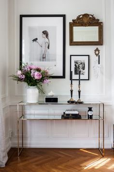 a console table with flowers and pictures on the wall