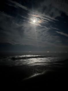 the moon shines brightly over the ocean on a dark night with clouds and waves