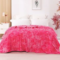 a bed with a pink blanket on top of it next to a white dresser and potted plant