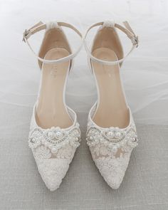 "Crochet style pointy toe heels with added small pearls applique and detachable ankle strap. Elegance and vintage inspired wear for your special day. DETAILS: HEELS: 3 inches COLORS AVAILABLE: Ivory and White UPPER: Synthetic upper and lining MATERIALS: Mandmade outsole ORIGIN: Imported STYLE NAME: EVA Not sure of which size to purchase? Shoes measurements are as follow: (Please note measurements taken the length of inside of shoe from toe to heel). Size 6 - 9.50\" Size 7 - 10.\" Size 8 - 10.25\ Elegant Low Heel Wedding Shoes With Lace Trim, Closed Toe Wedding Shoes With Lace Trim, Pearl Embellished Closed Toe Wedding Shoes, Pearl Embellished Closed Toe Wedding Shoes For Ceremony, Cream Lace Pointed Toe Wedding Shoes, Elegant Wedding Heels With Lace Trim, Elegant Wedding Shoes With Lace Work, Elegant Wedding Shoes With Lace Trim, Pearl White Pointed Toe Wedding Shoes