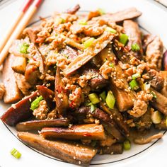 a white plate topped with meat and veggies next to two chopsticks