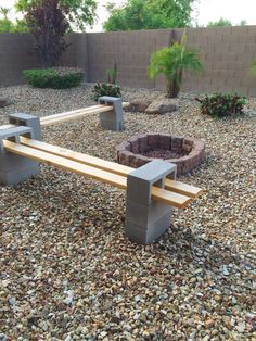 a wooden bench sitting in the middle of a gravel covered yard next to a fire pit