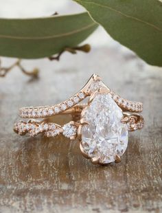 a close up of a ring with a pear shaped diamond in the center on a wooden surface