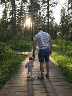 a man holding the hand of a small child on a wooden walkway in a forest