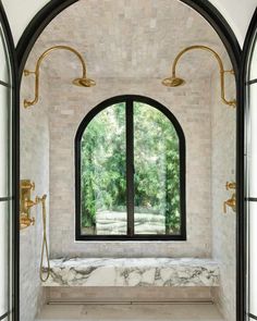 an arched window in a bathroom with marble and brass fixtures