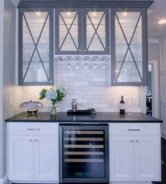 a kitchen with white cabinets and black counter tops, wine glasses on the cabinet doors