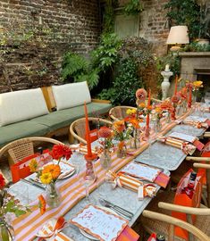 an outdoor dining area with orange and white striped tablecloths, place settings and flowers