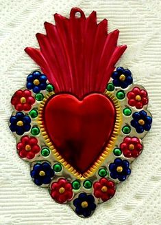 a red heart shaped ornament hanging on a white surface with flowers and beads