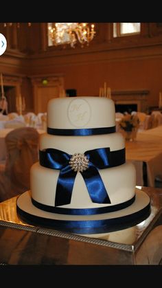 a three tiered wedding cake with blue ribbon and jewel brooch sits on a table