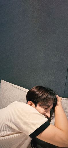 a woman laying on top of a white couch next to a black wall and holding her head in her hands