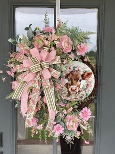 a wreath with pink flowers and a cow on it is hanging from the front door