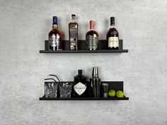 two black shelves with liquor bottles and glasses on them next to each other in front of a gray wall