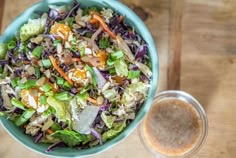 a green bowl filled with salad next to a cup of coffee on top of a wooden table