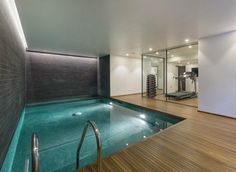 an indoor swimming pool in a home with wood flooring and glass doors leading to the gym