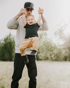 a man holding a small child up in the air while standing on top of a field