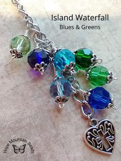 a close up of a bracelet with charms on it and the words island waterfall blues & greens