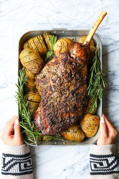 a person holding up a roasting pan with potatoes and meat in it on a marble surface