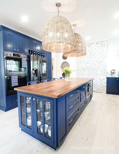 a large kitchen with blue cabinets and wooden counter tops, hanging lights over the island